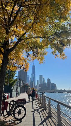 people are walking along the waterfront in front of the water and trees with yellow leaves