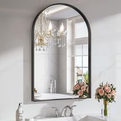 a bathroom sink sitting under a mirror next to a vase with flowers on top of it