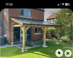 a wooden gazebo sitting on top of a lush green field next to a brick building