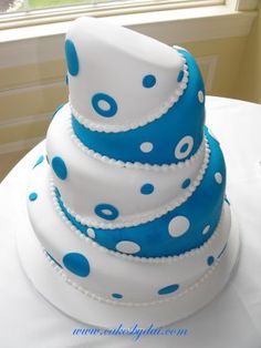 a three tiered cake with blue and white polka dots on the top is sitting on a table in front of a window