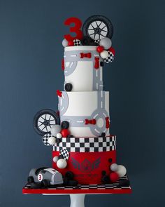 a three tiered cake with cars and wheels on the top is decorated in white and red