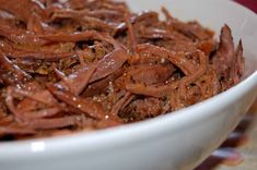 a white bowl filled with shredded meat and brown sauce on top of a tablecloth