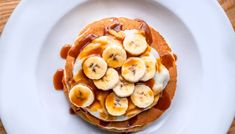 pancakes topped with bananas and whipped cream on a white plate