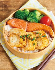 a wooden bowl filled with rice, fish and broccoli next to chopsticks