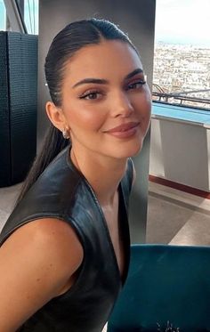 a woman wearing a black leather vest and smiling at the camera with a city in the background