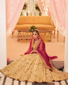 a woman in a yellow and red bridal gown sitting on the floor with pink drapes