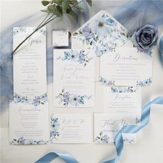 the wedding stationery is laid out with blue ribbons and flowers on it, along with a flower bouquet