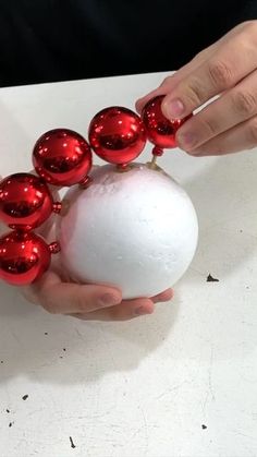 a person is holding a white ball with red ornaments on it and some hands are around it