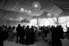 a group of people standing around tables in a room with drapes on the ceiling