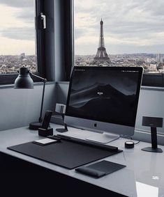 a desktop computer sitting on top of a desk in front of a window with the eiffel tower in the background