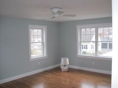 an empty room with two windows and a ceiling fan