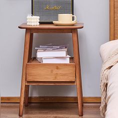 a small wooden table with books and a cup on it, next to a bed