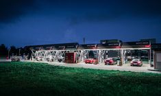 several cars are parked in front of a gas station at night with the lights on