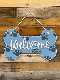 a welcome sign hanging on the side of a wooden wall with blue and white paw prints