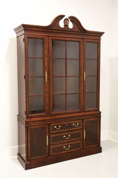 an antique china cabinet with glass doors and gold hardware on the bottom, against a white wall