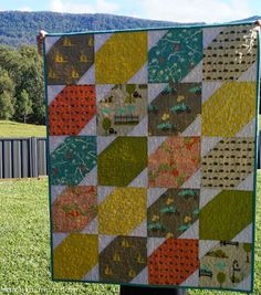 a patchwork quilt is hanging on a pole in the grass with mountains in the background