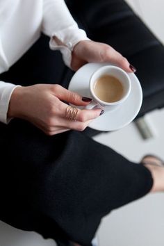 a woman is holding a cup of coffee in her hand and sitting on a chair