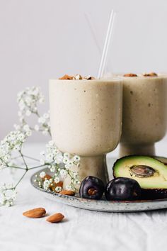 an avocado smoothie is served in two cups with almonds on the side