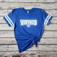 Introducing my Vikings school spirit lightweight jersey LAT tees, the perfect blend of softness, stretchiness, comfort, and cuteness! These tees are designed to elevate your school spirit wear to new levels of style and comfort. Crafted from high-quality lightweight material, these tees offer an exceptional softness that feels gentle against your skin. Embrace the comfort of these shirts, as they provide a cozy and luxurious feel that you'll never want to take off. The stretchy fabric ensures a Collegiate Style School T-shirt With Screen Print, Blue College T-shirt For Football Season, School Spirit Tops For Football Season, Casual T-shirt For School Football Season, College T-shirt With School Spirit, College Football Season School Spirit T-shirt, Casual School T-shirt For Football Season, Cotton T-shirt For College Football Season, Blue Top For College Football Season