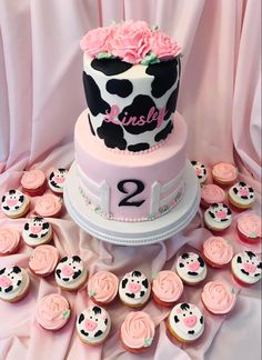 a pink and black cow themed cake surrounded by cupcakes