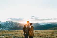 two people standing on top of a grass covered field with mountains in the back ground