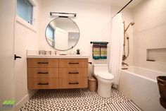 a white toilet sitting next to a bath tub under a bathroom mirror on top of a wooden cabinet