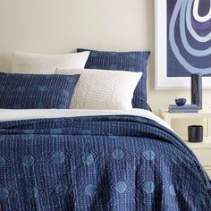 a bed with blue and white comforters in a bedroom next to a painting on the wall