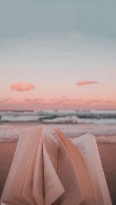 an open book sitting on top of a sandy beach next to the ocean at sunset