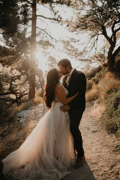 a bride and groom standing together in the woods