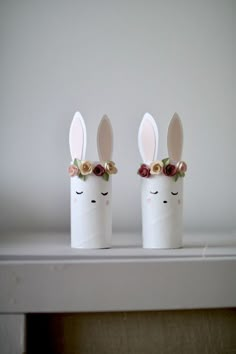 two white vases with bunny ears and flowers on them sitting on top of a shelf