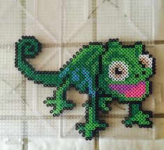 a cross stitch pattern of a green and pink lizard on a white tile wall,