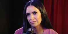 a woman with long black hair is holding a microphone and looking at the camera while standing in front of a red curtain