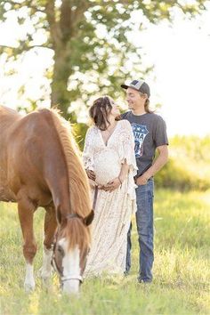 a pregnant woman standing next to a brown horse in a field with her husband looking on