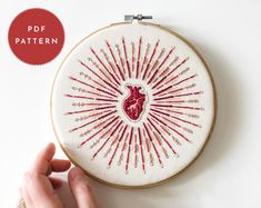 a hand is stitching a heart on a white wall hanging from a hoop with red thread