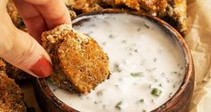 a person dipping something into a bowl of ranch dip with chicken wings in the background