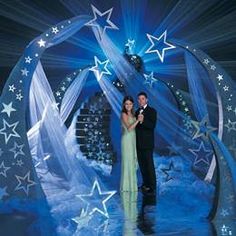 a man and woman standing in front of a stage with stars on the wall behind them