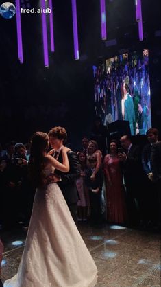 two people are dancing in front of an audience at a formal event with purple lights