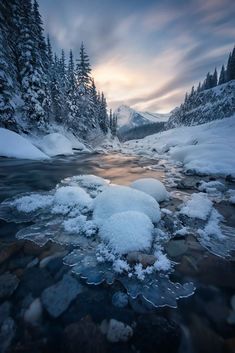 the sun is setting over a mountain stream with ice and snow on it's banks