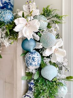 an arrangement of blue and white ornaments on a fireplace mantel with greenery in the foreground