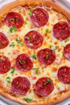 a pepperoni pizza on a white plate with parsley sprinkled on top