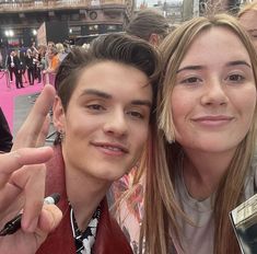 two people posing for the camera in front of a pink carpeted area with lots of people