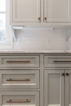 a kitchen with white cabinets and gold handles