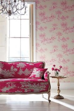 a pink couch sitting in front of a window next to a table with flowers on it