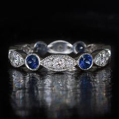 a white gold ring with blue sapphires and diamonds on the side, sitting on a reflective surface