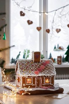 a gingerbread house on a table in front of a window with christmas lights around it