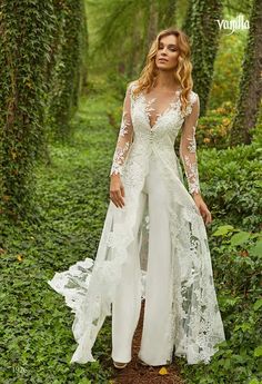 a woman standing in the middle of a forest wearing a white wedding gown with long sleeves