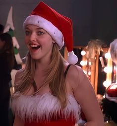 a woman wearing a santa hat and red dress in front of christmas lights with her mouth open