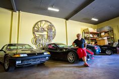 a man sitting on the hood of a car in a garage next to two other cars