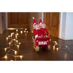 two elfs riding in a red wagon with lights on the floor next to them