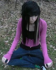 a young woman sitting on the ground with her hands in her pockets and looking down